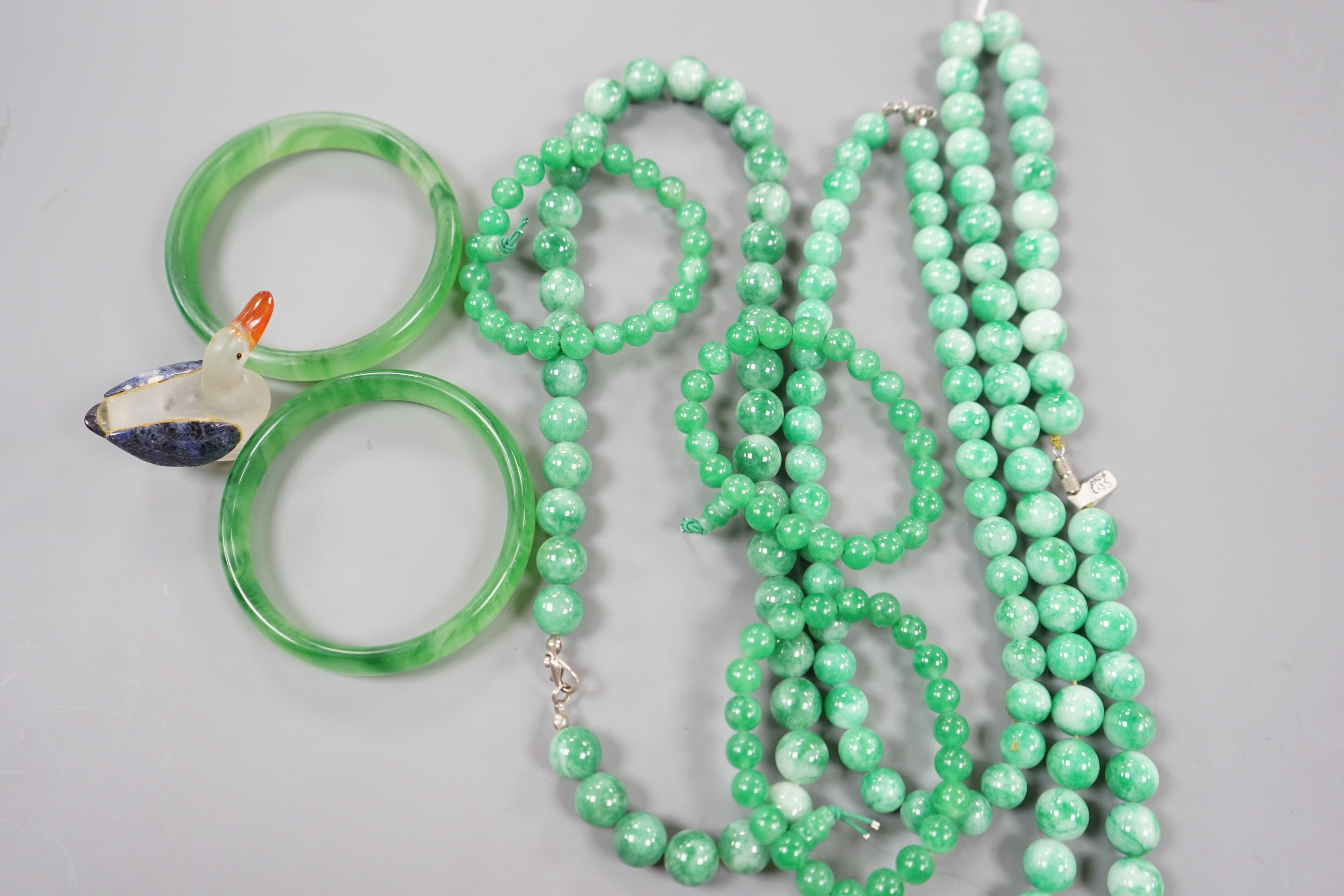 A group of three jadeite necklaces, together with two jadeite bracelets, two green glass bangles and a glass figure of a duck (8)